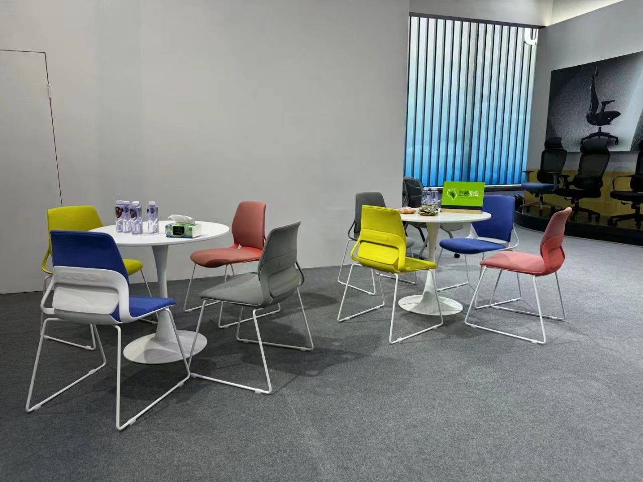 Modern visitor chairs in vibrant colors arranged around round tables, perfect for reception areas or casual meeting spaces.