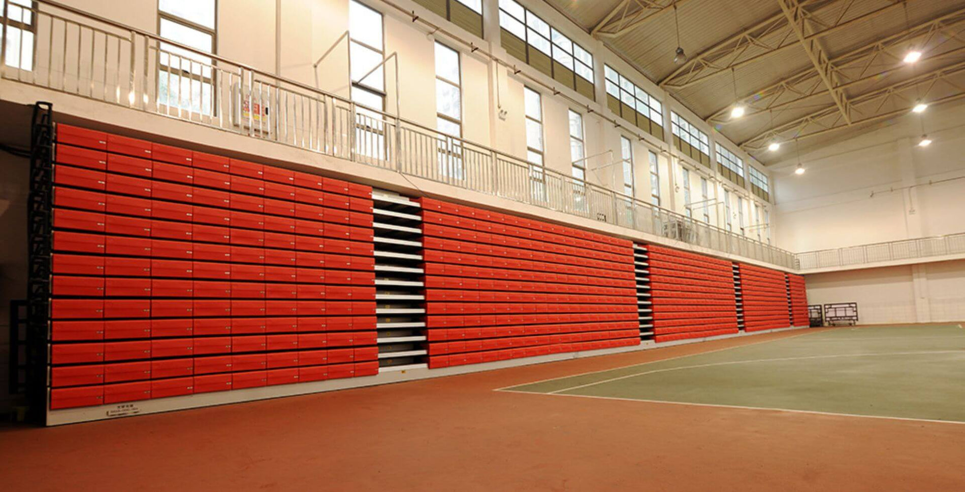 Telescopic gym bleachers with red seats, featuring a retractable design, metal supports, and installed on a polished wooden floor